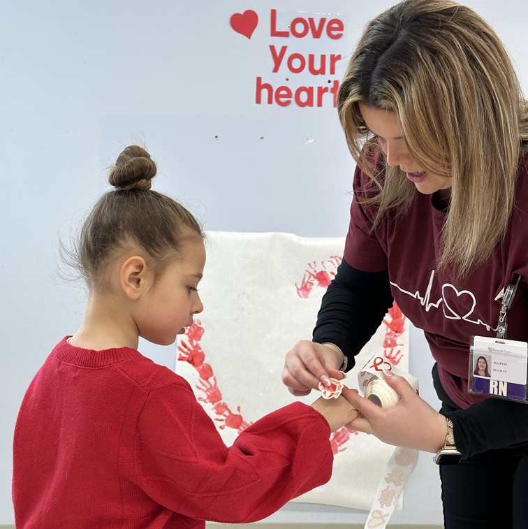 A Post Avenue Teacher gives a student a heart sticker for Wear Red Day.